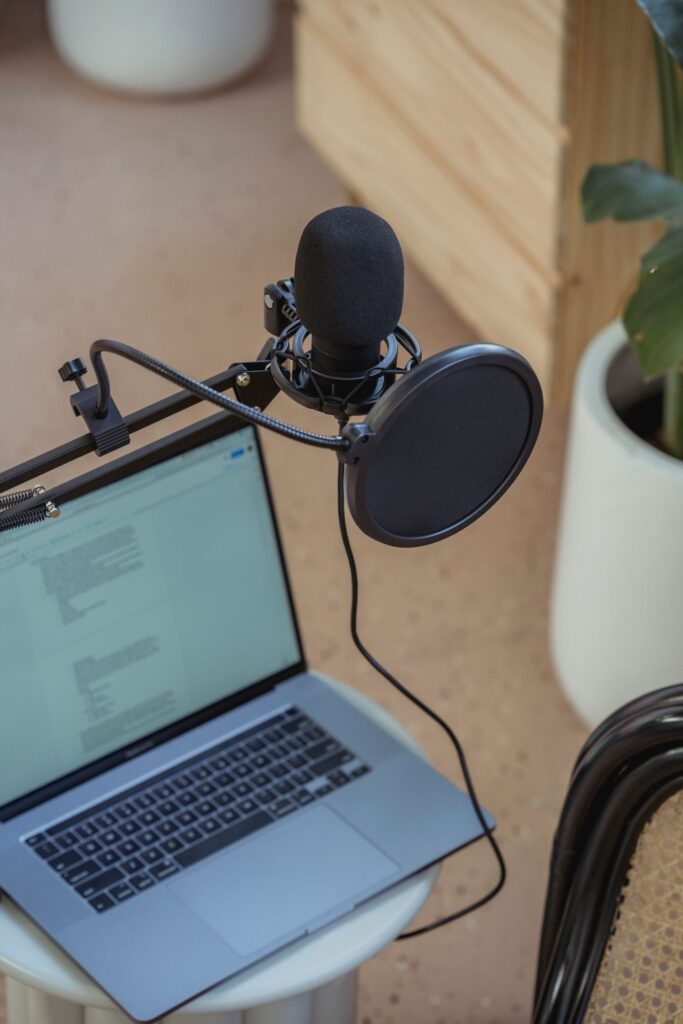 From above of modern opened laptop with microphone on tripod placed on small table near chair during recording radio program